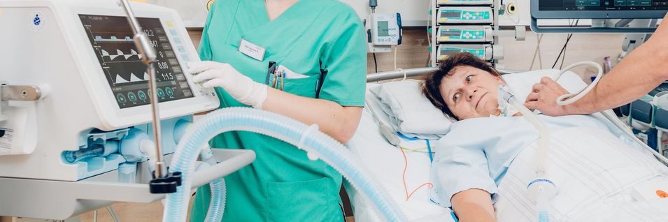 Arzt am Bett bei Behandlung einer Patientin; Krankenschwester bedient medizinisches Gerät