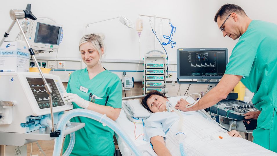 Arzt am Bett bei Behandlung einer Patientin; Krankenschwester bedient medizinisches Gerät